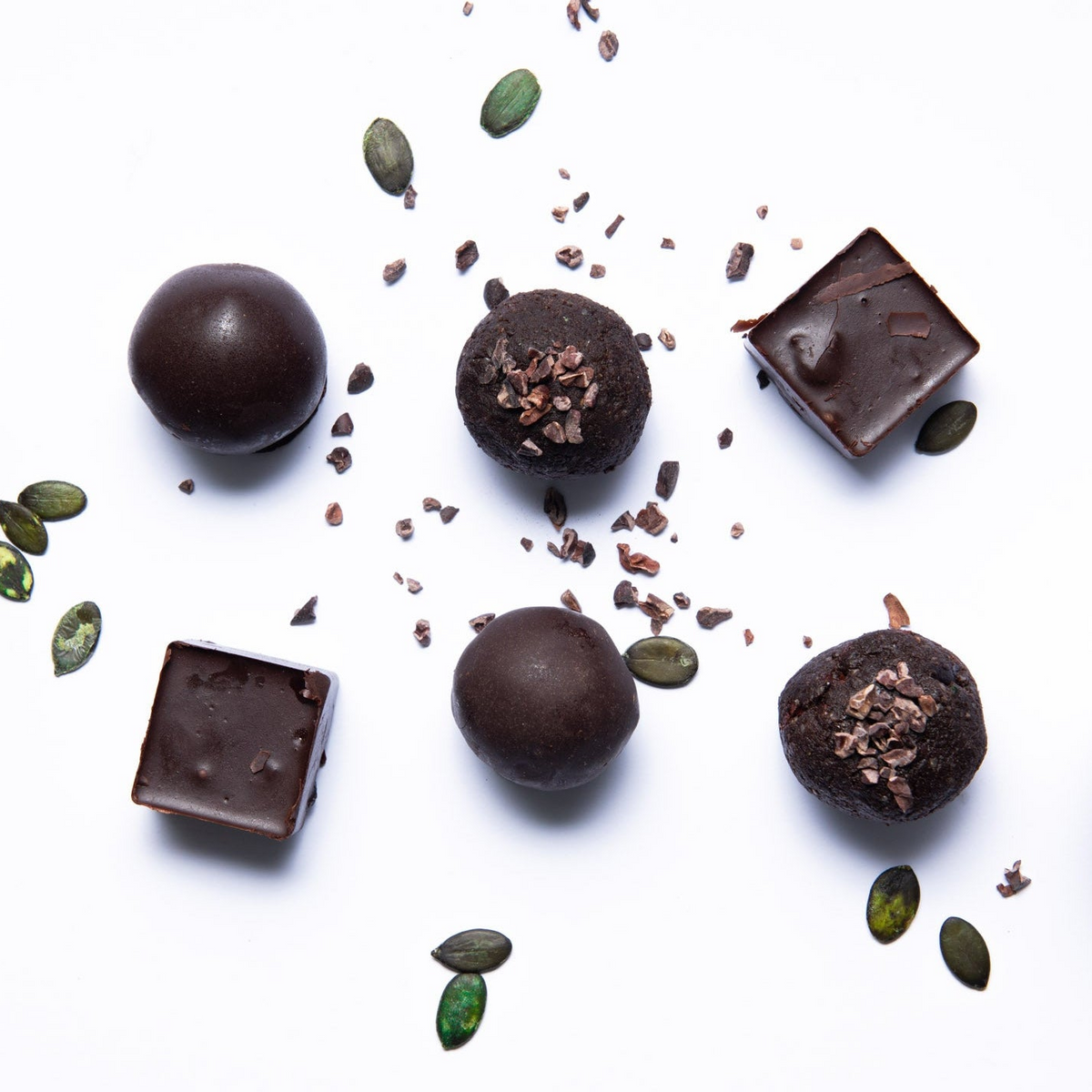 Dark chocolate truffles with pumpkin seeds and cacao nibs on a white background